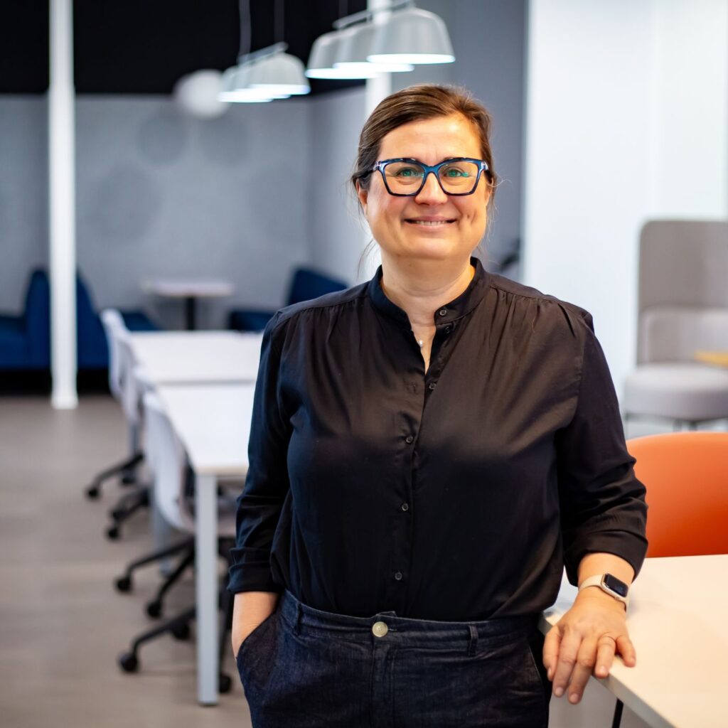 Členka týmu Sales House Group stojí v moderní kanceláři a reprezentuje přátelské i profesionální pracovní prostředí firmy.