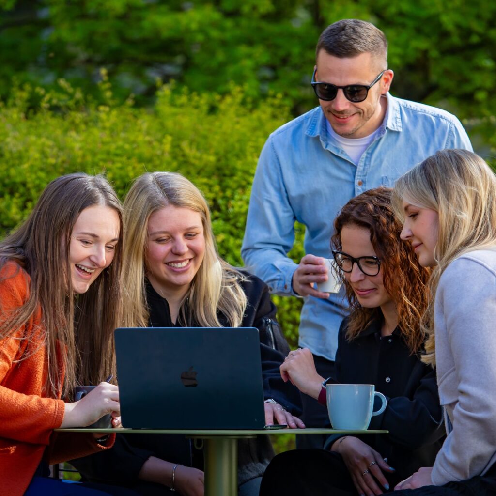 Členové týmu Sales House Group společně pracují u notebooku venku a ukazují týmovou spolupráci v neformální atmosféře.