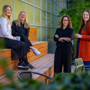 Čtyři členky týmu Office & Vývoj ze Sales House Group v uvolněné atmosféře na dřevěných stupních v moderním atriu budovy.