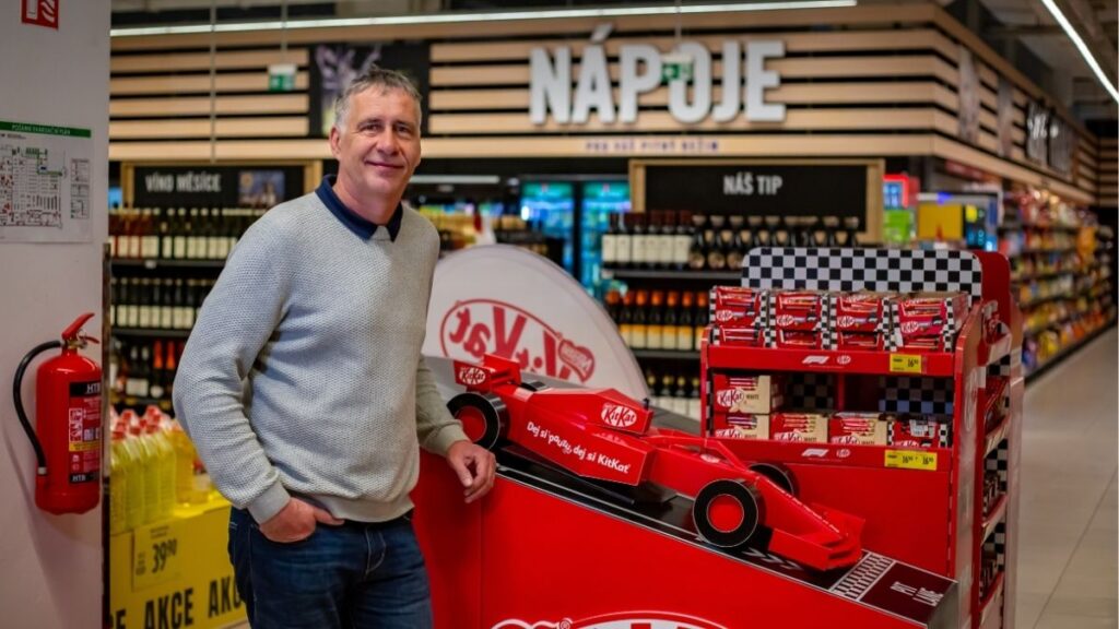 Člen týmu Sales House Group stojí u promo vystavení v prodejně a představuje práci v oblasti merchandisingu, sales a podpory prodeje v retailu.